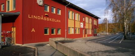 En röd skolbyggnad i trä med texten Lindåsskolan på fasaden