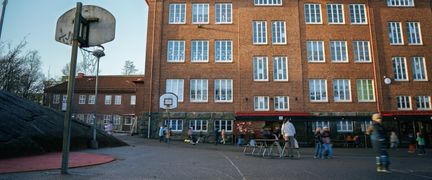 Lundenskolans huvudbyggnad med några personer och ett par basketkorgar i bakgrunden.