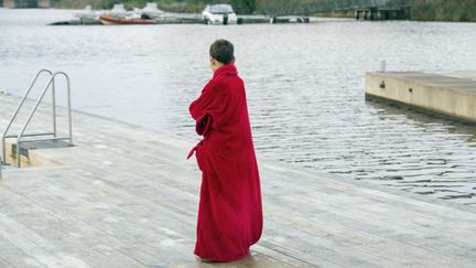 En person står med röd morgonrock för att ta ett dopp efter bastun