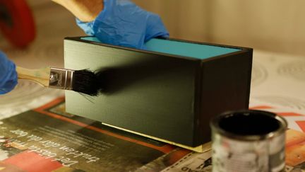 En person målar en trälåda svart.