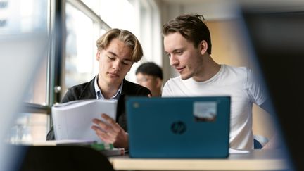 Två gymnasiekillar sitter och jobbar i ett klassrum.