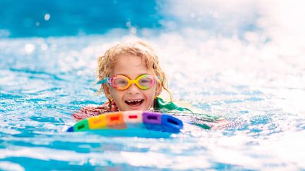 Ett barn som simmar i vattnet med färgglada simglasögon och en färgglad flytleksak