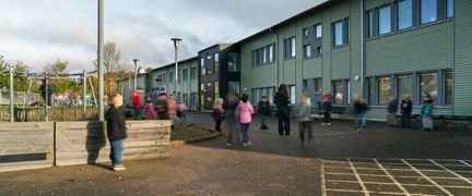 Elever och vuxna som står på skolgården utanför en skolbyggnad.