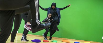Ett barn rör sig i en gymnastiksal tillsammans med vuxna.