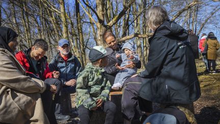 En grupp människor i olika åldrar sitter tillsammans ute i naturen.