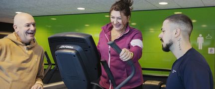  Två personer står vid en träningscykel tillsammans med en instruktör.