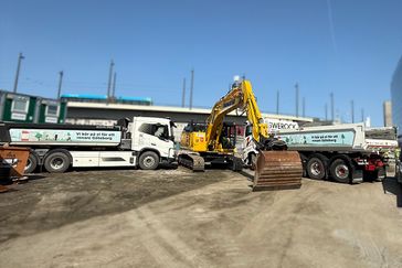 En byggarbetsplats med två eldrivna lastbilar och en gul grävmaskin i arbete. På lastbilarnas sidor står texten 'Vi kör på el för ett renare Göteborg