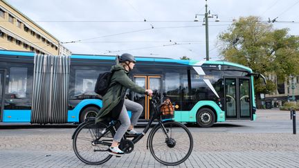 Tjej som cyklar med en buss i bakgrunde