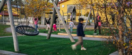Några elever som leker på en skolgård och en gul skolbyggnad i bakgrunden.