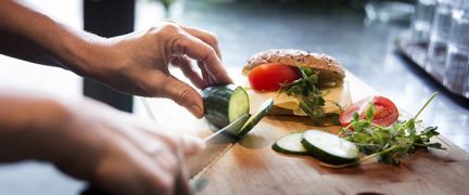 En person skär gurka till en smörgås.