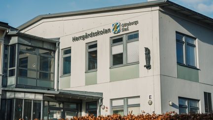 En stor vit skolbyggnad med texten Herrgårdsskolan Göteborgs Stad på fasaden.