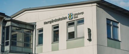 En stor vit skolbyggnad med texten Herrgårdsskolan Göteborgs Stad på fasaden.