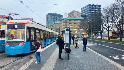 Spårvagn i ordinarie läge vid Järntorget, med busshållplats bredvid. Myller av människor på hållplatsen. Mashuggskajens byggnation med Våghuset i bakgrunden.