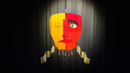 En svart upplyst ridå med en teatermask där halva är glad och halva ledsen. 