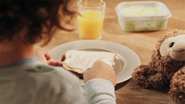 ett barn sitter vid frukostbordet och brer en smörgås