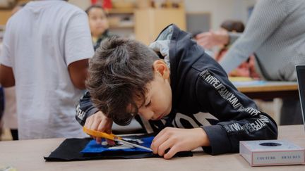  Ett foto av ett barn som klipper tråd på en tygbit i en textilslöjdssal.