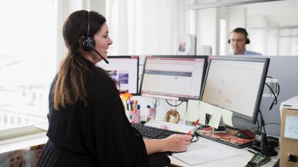 Två personer jobbar vid sina skrivbord med headset på i kontorsmiljö
