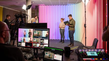 En inspelning med en scen där det står två personer och filmare och i förgrunden en tekniker framför en datorskärm.