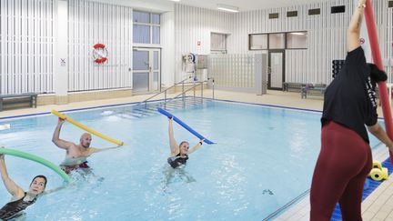 Tre personer deltar på vattengymnastik och följer ledarens rörelser.