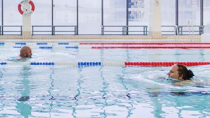 Två personer simmar i simhallen