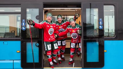 Tre hockeyspelare i matchkläder står i dörren till en spårvagn.
