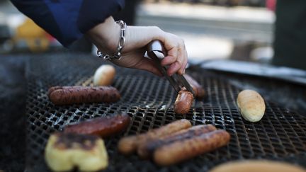 En närbild på en hand som grillar korv och bröd 