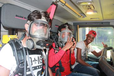 Tre ungdomar sitter med rökdykningsmask i ett utryckningsfordon och gör tummen upp.