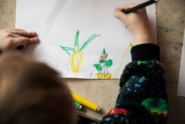 Ett barn ritar en teckning i grönt och gult.