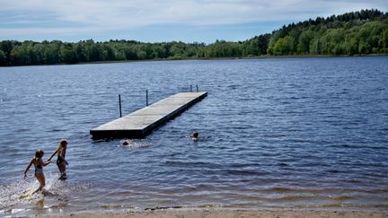 Bild på en sjö med en brygga och barn som badar.