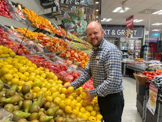 En ICA-handlare står vid vid fruktavdelningen och ler mot kameran.
