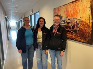 Tre kvinnor står i en korridor och ler mot kameran