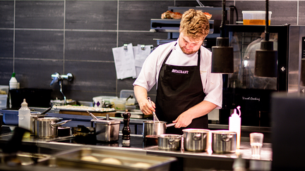 En kock som står i ett restaurangkök och vispar i en gryta.