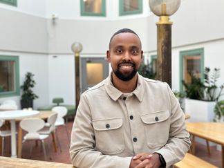 En man ler in i kameran. han befinner sig i en kontorsmiljö. 