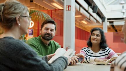 En grupp människor sitter vid ett bord och samtalar om en bok