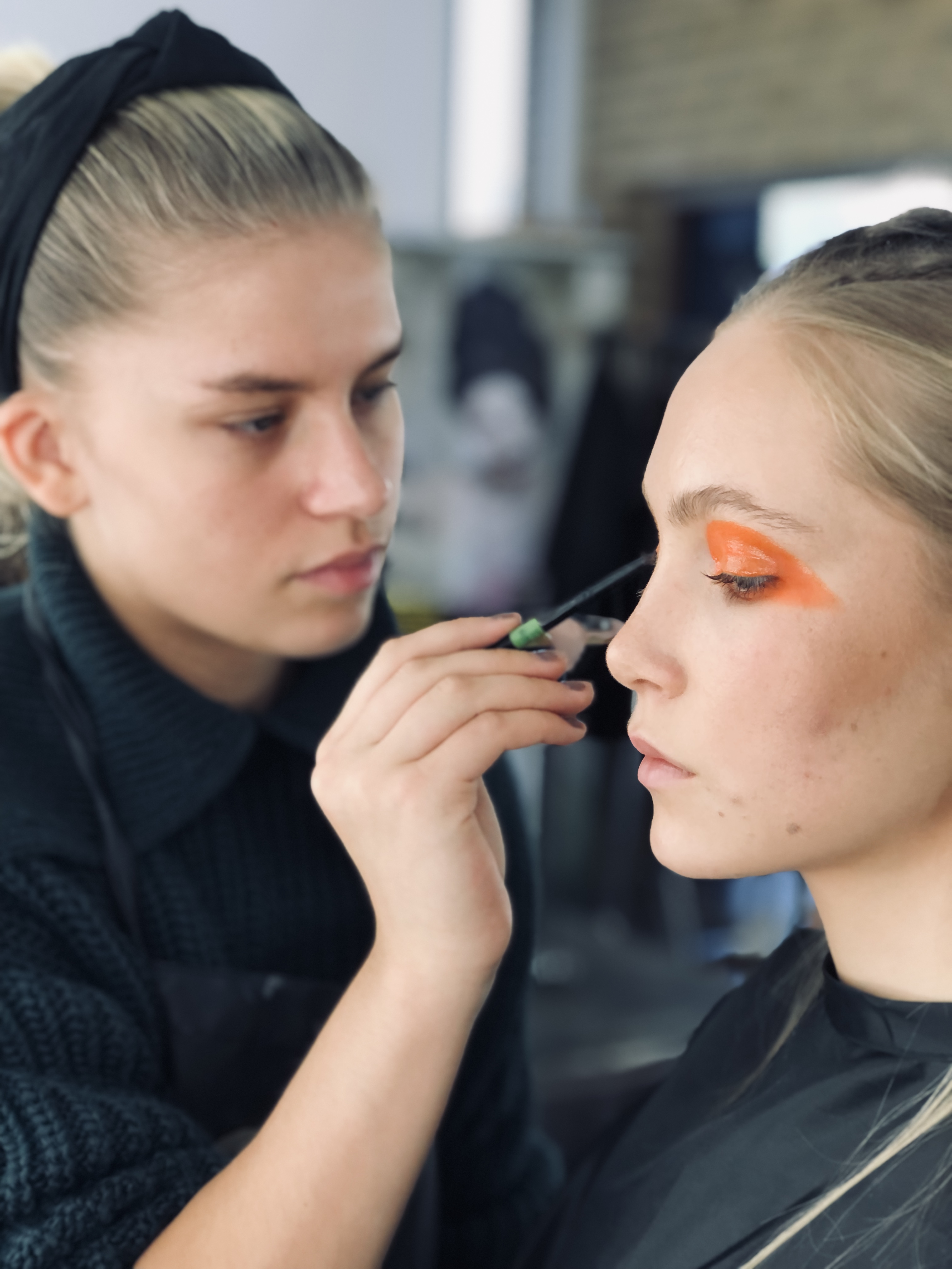 En person målar orange ögonsminking på en modell.