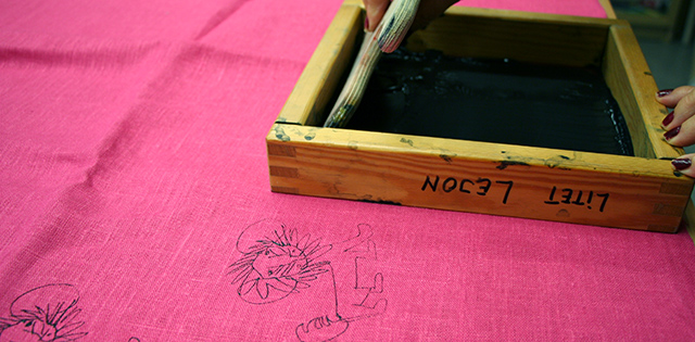 Närbild på rosa tyg med ett svart lejon tryckt på. I bakgrunden syns en träram som det står "litet lejon" på