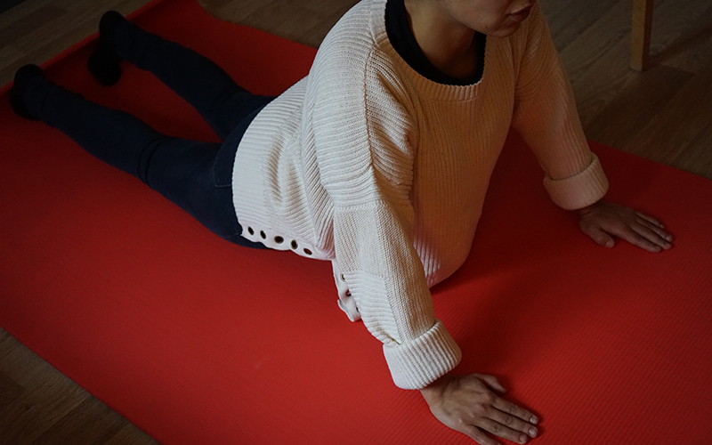 Person ligger på mage på en röd yogamatta och gör en stretchövning.