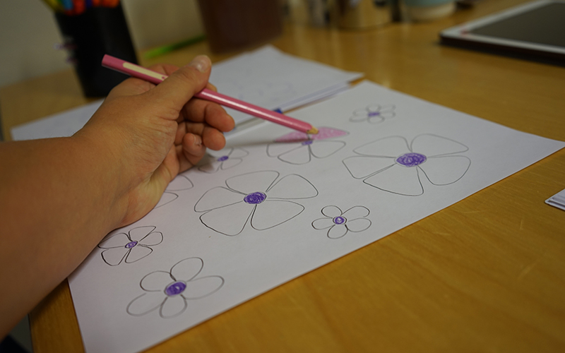 Hand som håller i en penna och ritar blommor på ett papper.