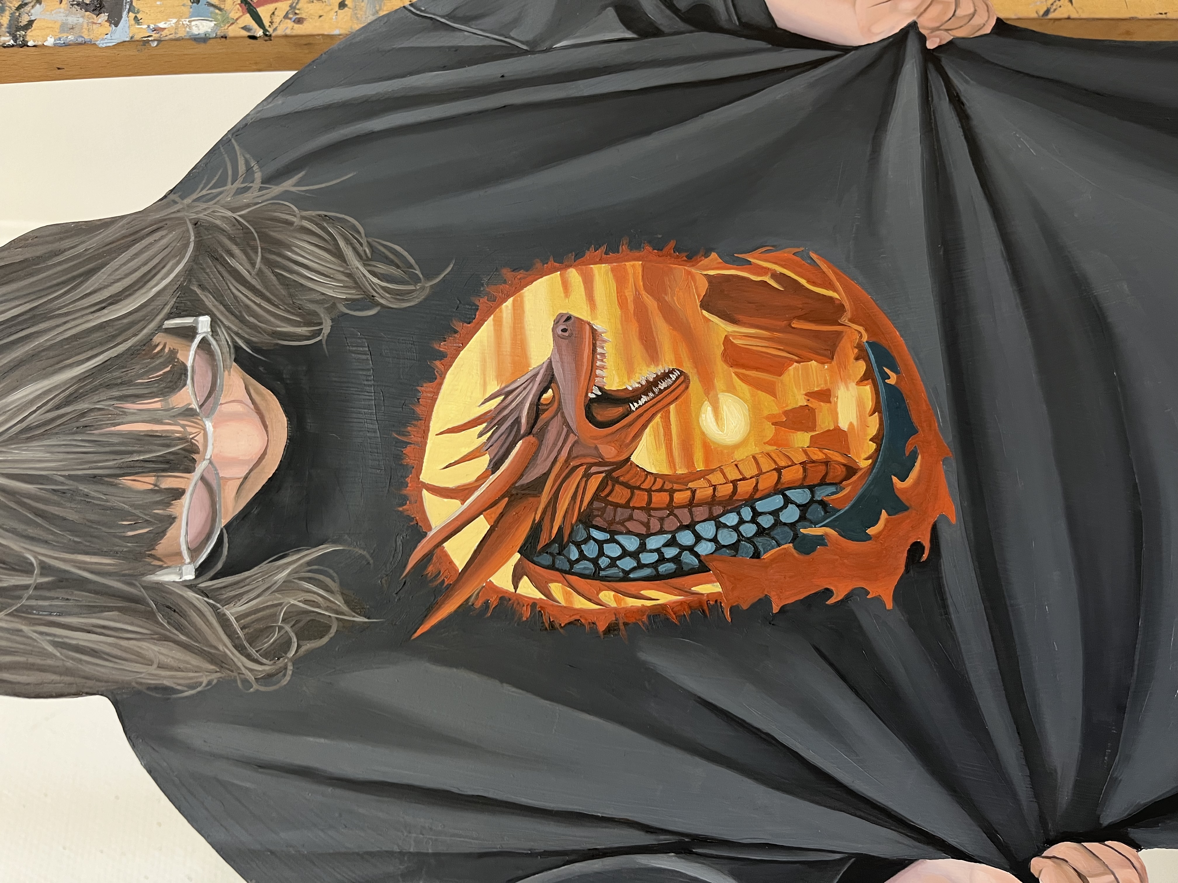 Närbild på ett konstverk gjort av trä som är målad p. Figuren är en person som tittar ner i marken och har på sig en svart t-shirt med en drake på.