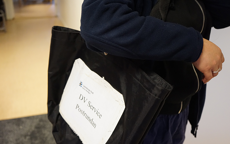 Person sedd från sidan med en axelremsväska med post i.