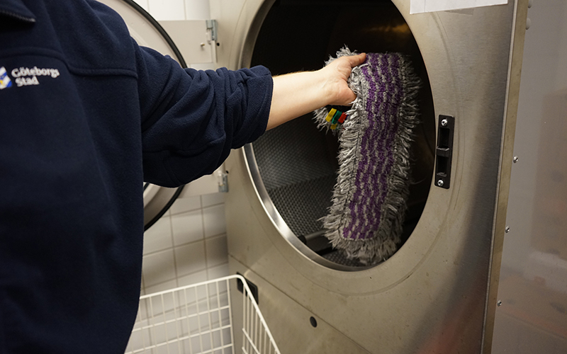 En person lägger in en mopp i en tvättmaskin.