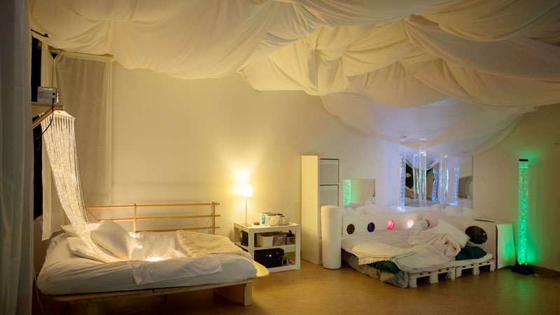 Ett rum. I rummet finns flera färgglada lampor och två sängar. I taket hänger vita draperier.